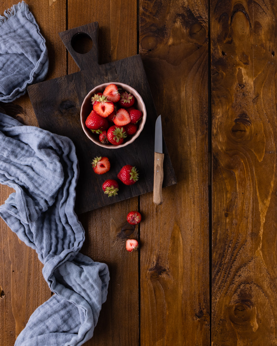 Vinyl Backdrop Motiv Echtholz braun mit einer Schale voll Erdbeeren für Fotografie. Veredelt wurde das Bild mit einem, grauen Tuch und einem Holzbrettchen aus Eiche. Dieser Fotohintergrund eignet sich sowohl für Produktfotografie als auch für Foodfotografie.