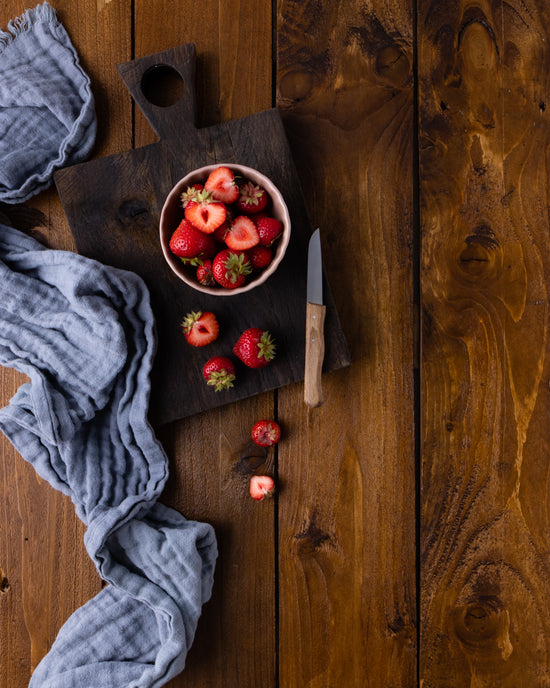 Vinyl Backdrop Motiv Echtholz braun mit einer Schale voll Erdbeeren für Fotografie. Veredelt wurde das Bild mit einem, grauen Tuch und einem Holzbrettchen aus Eiche. Dieser Fotohintergrund eignet sich sowohl für Produktfotografie als auch für Foodfotografie.